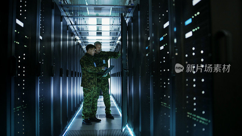 在数据中心，两名军人使用开放式服务器机架机柜工作。一个是军用版笔记本电脑。