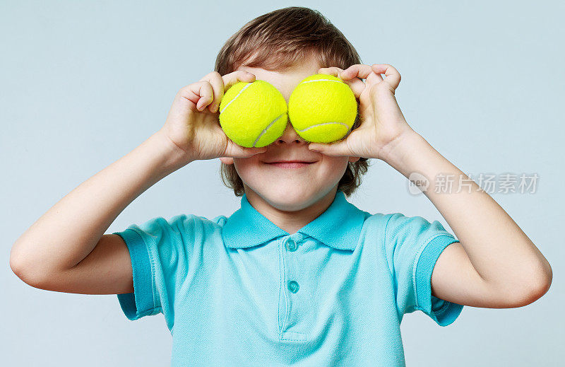小男孩拿着网球而不是眼睛，微笑着