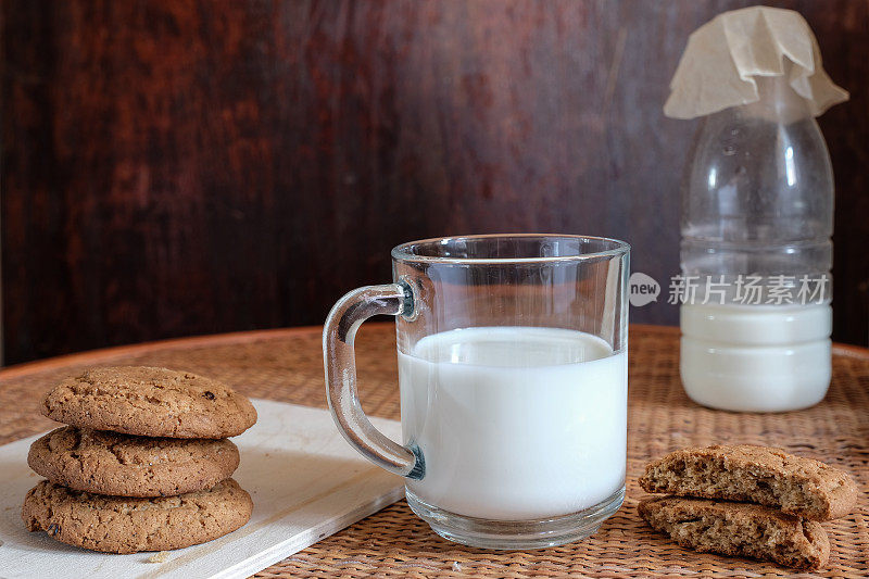 乡村早餐，一杯牛奶和圆燕麦饼干一个放在另一个，碎燕麦饼干一半，旁边是一瓶牛奶在黑暗的背景