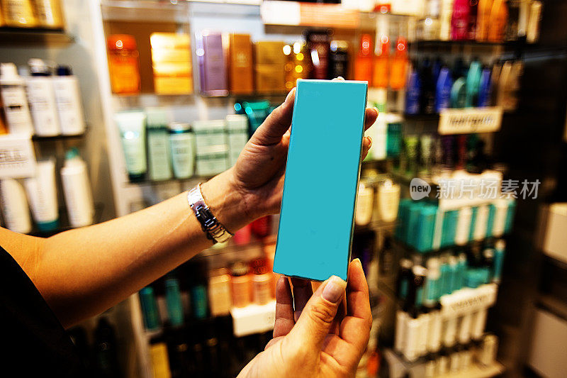 在化妆品商店的过道里，一名女士的手拿着一个蓝色的盒子