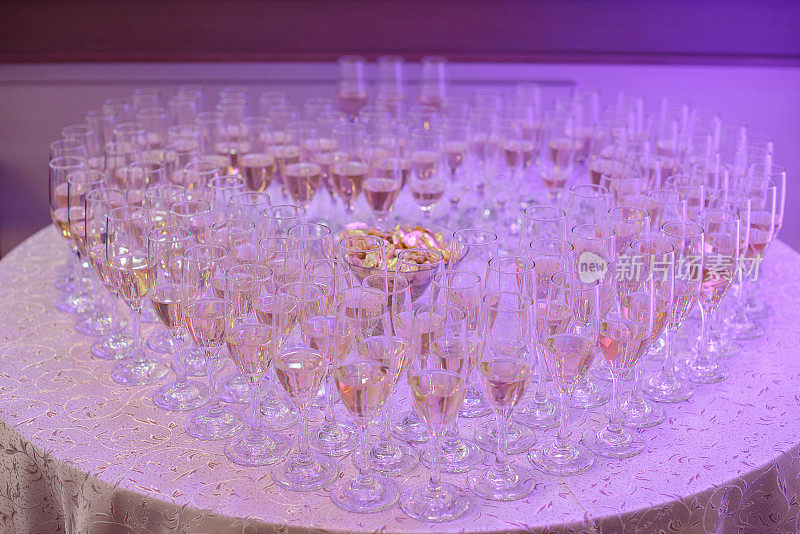 满杯的起泡酒或香槟呈心形，放置在紫色霓虹灯下的圆桌上，这是典型的婚宴或欢迎客人、家人和朋友的派对