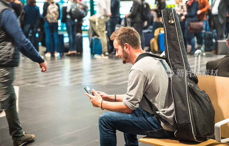 在国际机场使用手机的潮人-在候机楼门口等待飞机的人-带着吉他背包的旅行概念-专注于脸