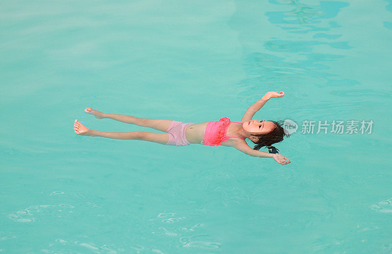 小女孩在游泳池的水面上漂浮着。