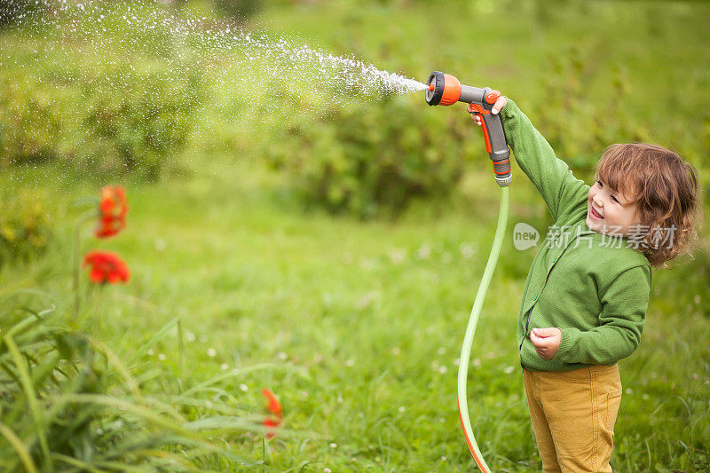 蹒跚学步的女孩玩得很开心。给花园浇水
