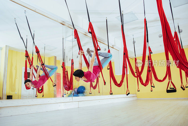 年轻女性在工作室做瑜伽运动或空中瑜伽反重力。