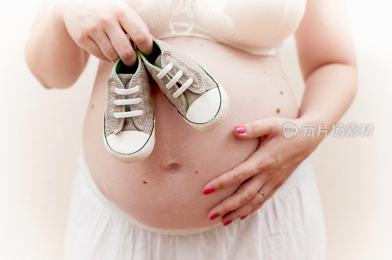 抱着一双婴儿鞋的孕妇