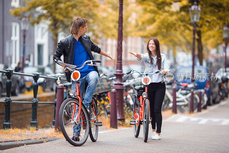 年轻幸福的白人夫妇在阿姆斯特丹的老街上骑自行车