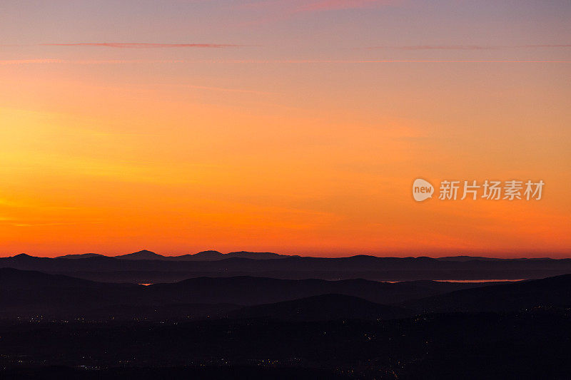 美丽的翁布里亚(意大利)山谷在黄昏的鸟瞰图，山丘，城市灯光和trasiimeno湖反射橙色的天空光