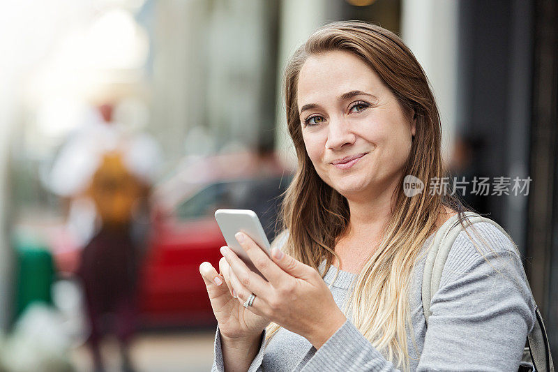 一个女人走在街上，一边发短信一边微笑