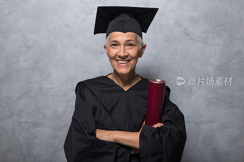 微笑的老女人在毕业礼服拿着大学文凭