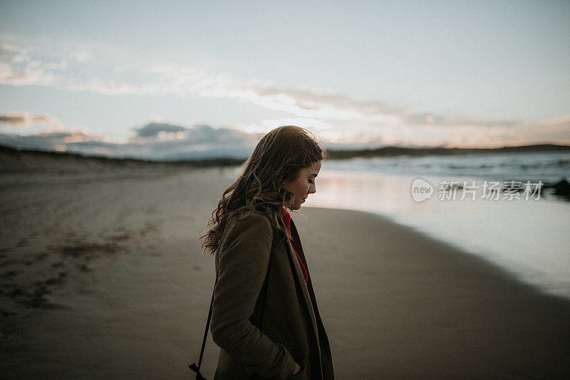 一个年轻女子在冬天的夕阳下走过海滩