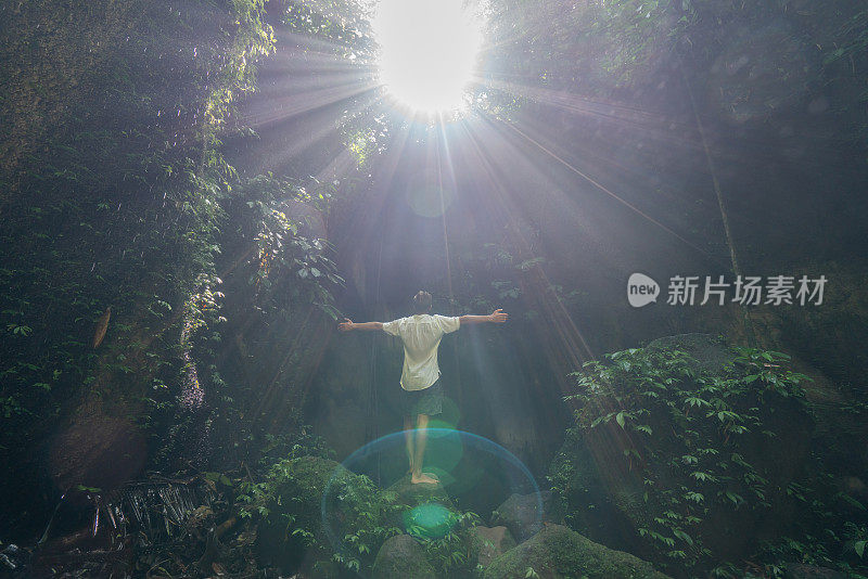 在巴厘岛的热带雨林中，一名旅行的年轻人张开双臂拥抱大自然的美丽。人们以自然为旅游理念。