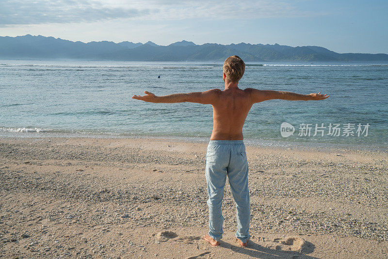 年轻人在海滩上伸开双臂享受热带气候和异国情调的假期。旅游目的地自由的人好奇的概念自然