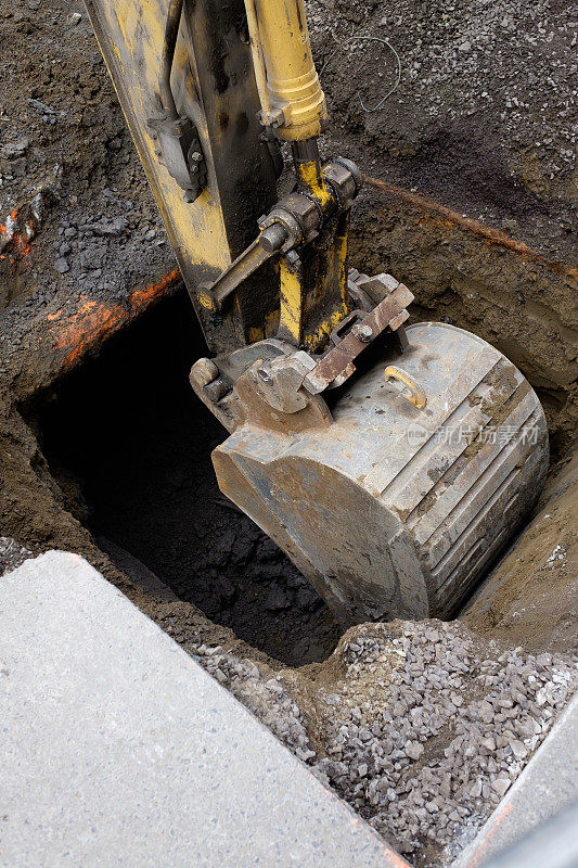 路边的街道上，一台黄色挖掘机的电铲正在地上挖洞。