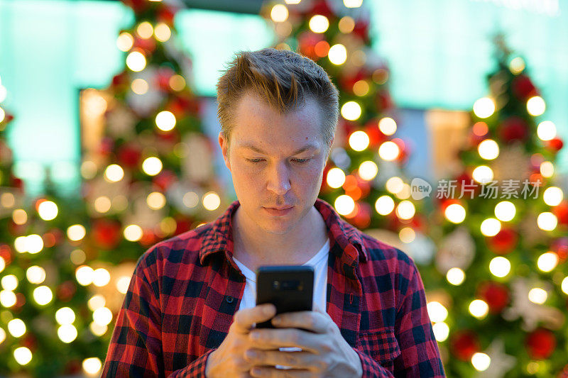 年轻帅气的嬉皮士在户外用手机对着圣诞树