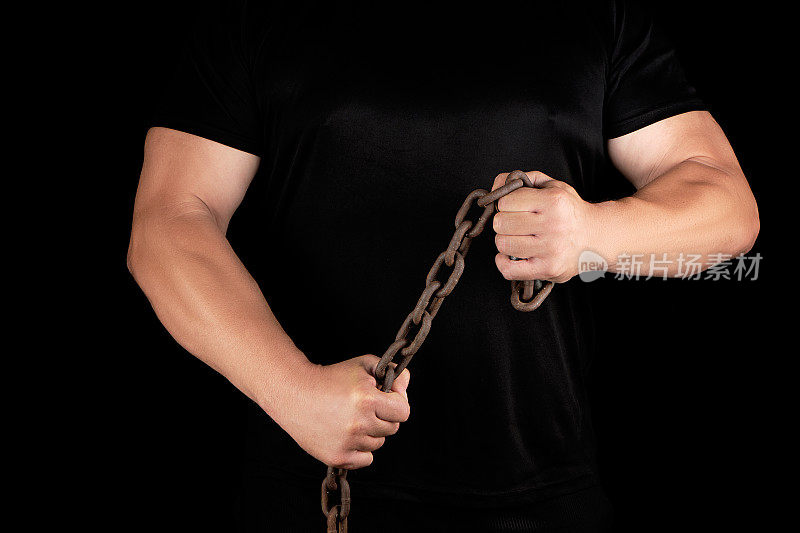 一个穿着黑衣的成年男子站得笔直，肌肉紧张，手里握着一根生锈的铁链