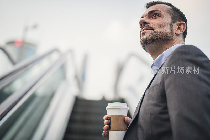 在城市的自动扶梯上拿着一次性杯子的商人