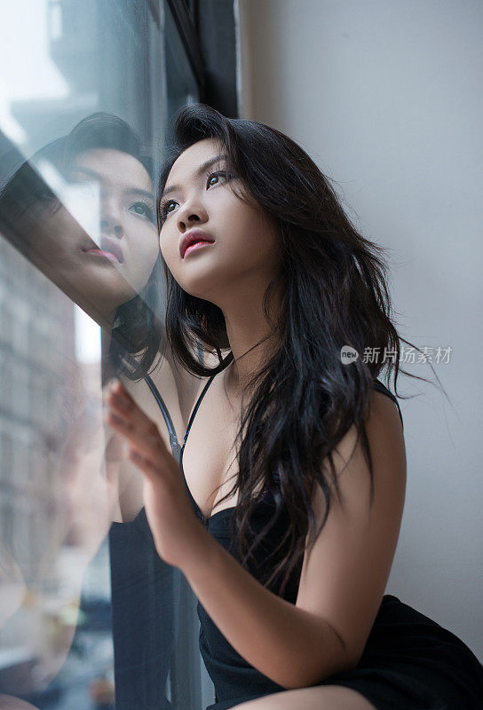 感性的亚洲年轻女子坐在窗前，望出去，情感肖像
