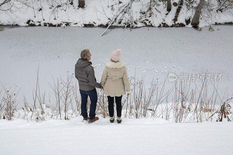 成熟的夫妇穿过雪走向河边