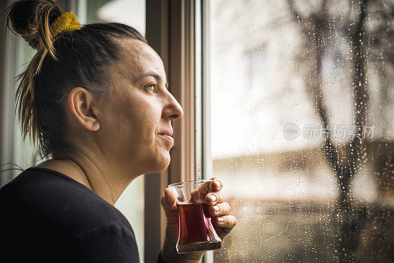 下雨天透过窗户看窗外喝茶的女人