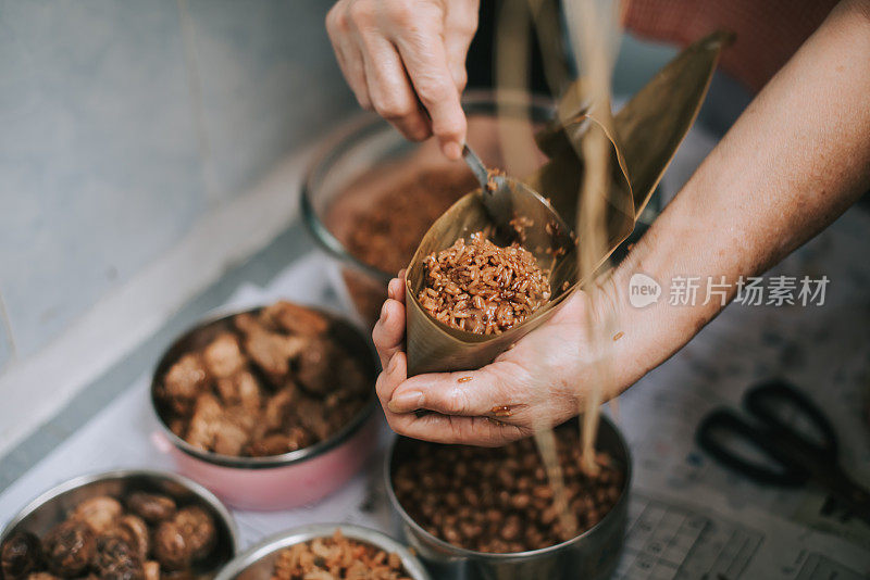 一位年长的亚洲华人妇女在她的厨房里准备粽子，把配料包好，为端午节做准备