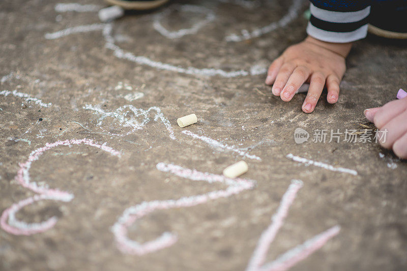 一个小男孩用彩色粉笔在柏油路上画数字