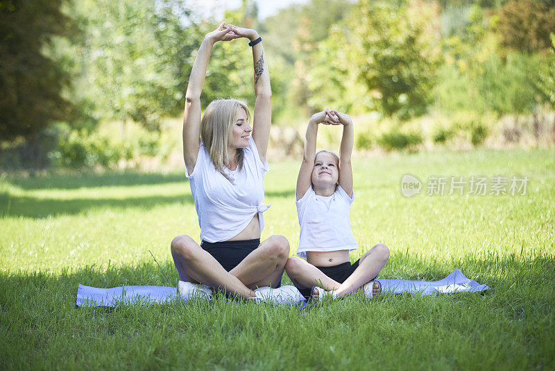 中年母亲练习瑜伽与蹒跚学步的女儿，美丽的母亲和女儿训练在一个夏天的一天户外。