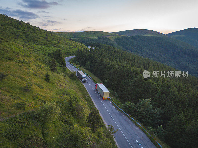 日落时分，快递公司的卡车载着货物行驶在山区的森林道路上。