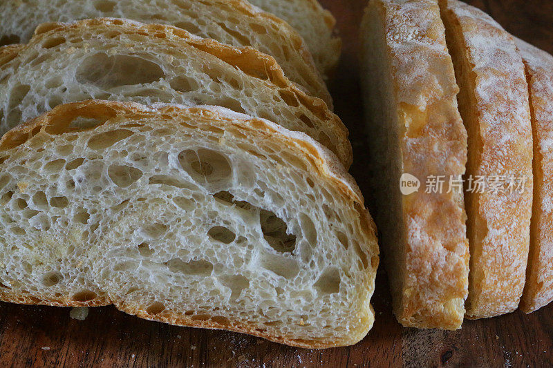 特写:切成薄片的自制夏巴塔面包，放在木砧板上，金黄色，刚出炉的面包，切成薄片的硬面包