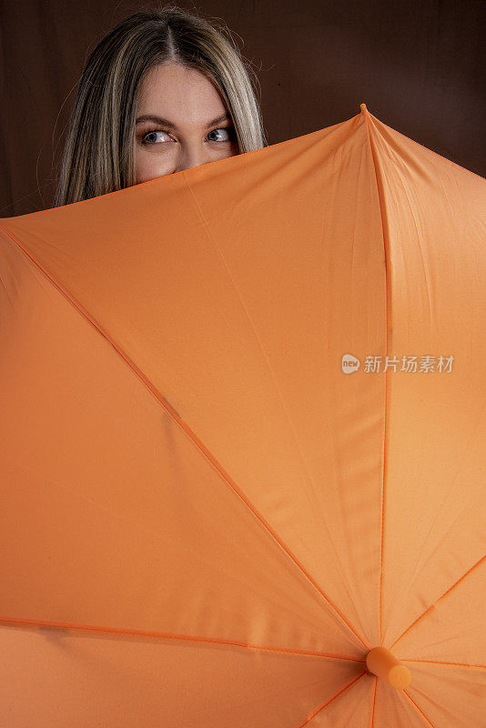 年轻女子拿着一把橙色的伞准备出门，看着镜头。