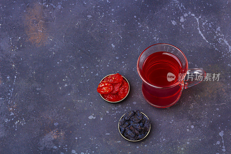 土耳其茶杯(armudu)红茶(roibos，木槿，karkade)和干果(山茱萸，葡萄干)在深色的背景上。草药，维生素，治疗感冒和流感的排毒茶。文本复制空间