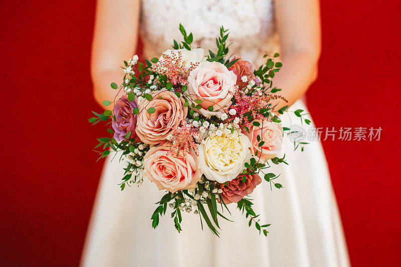 美丽的白色和粉红色的鲜花捧在迷人的新娘手中，穿着白色的裙子