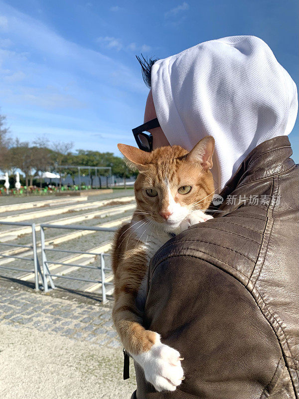 一个男人牵着一只姜黄色的猫走在街上