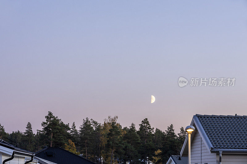 美丽的自然景观在一个夏夜。别墅的屋顶，森林，月亮，蓝天和云汇聚在地平线上。瑞典。