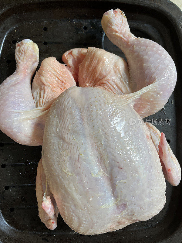 整只鸡放在厨房工作台上的烤箱托盘里，准备放在烤箱里烤，高架视野
