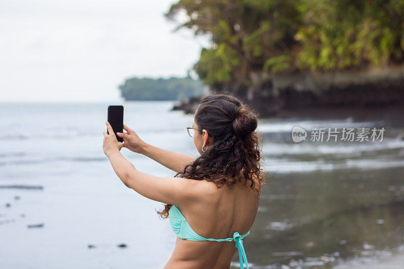 年轻女子在海边用智能手机自拍