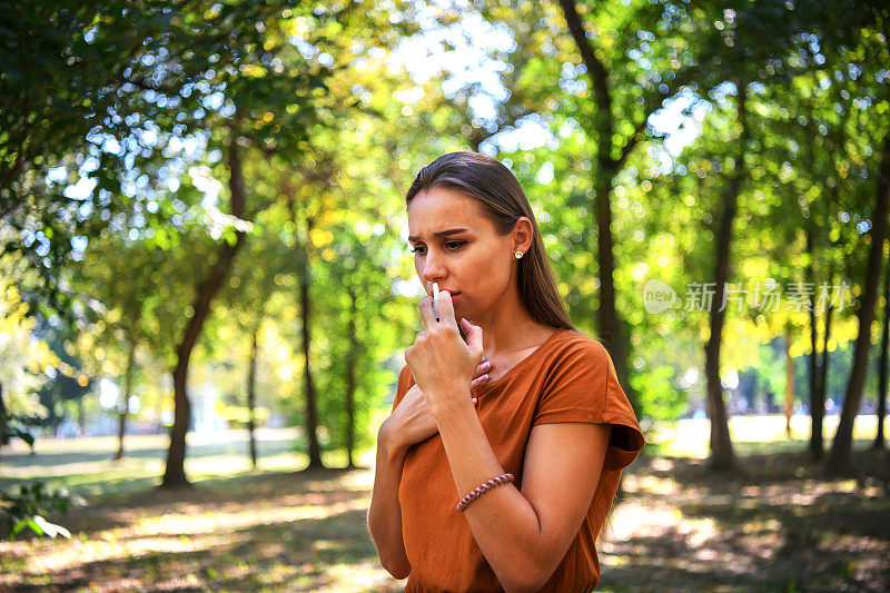 一位美丽的女人正在公园里使用鼻喷雾剂。