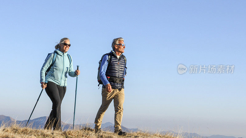 成年夫妇沿着长满青草的山脊徒步旅行