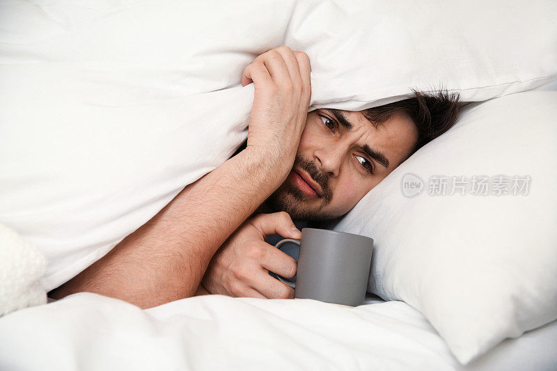 生病的年轻人在家里的床上喝着一杯热饮。流感病毒