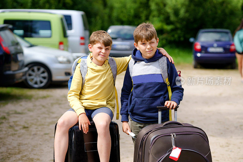 两个孩子，学弟学弟，在去夏令营之前坐在行李箱上。快乐的孩子，兄弟姐妹，双胞胎兄弟去旅行，家庭公路旅行