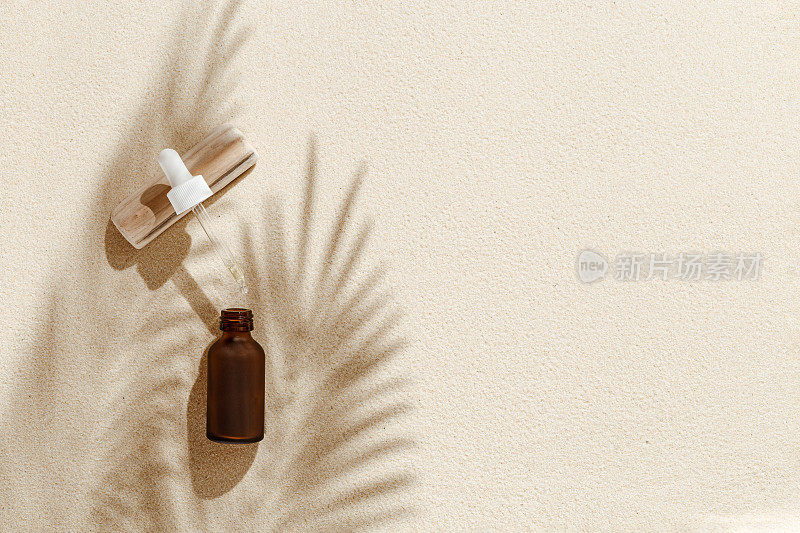 液体产品包装在深色玻璃瓶上的沙子背景与阳光和阴影从棕榈叶