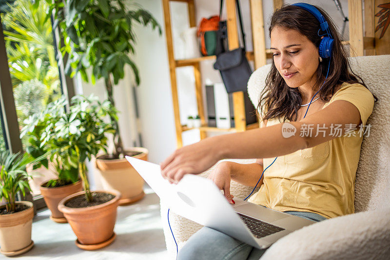 年轻女子戴着耳机在家使用笔记本电脑