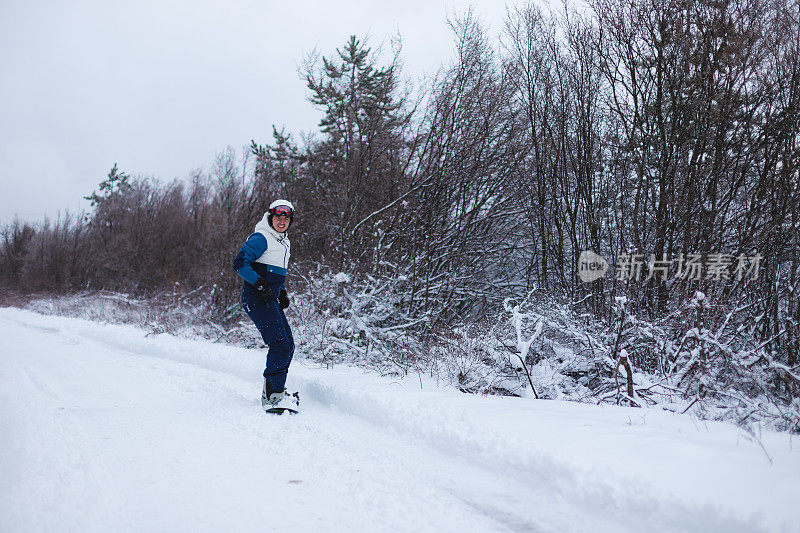 年轻的男性单板滑雪运动员从被雪树环绕的山坡上滑下来