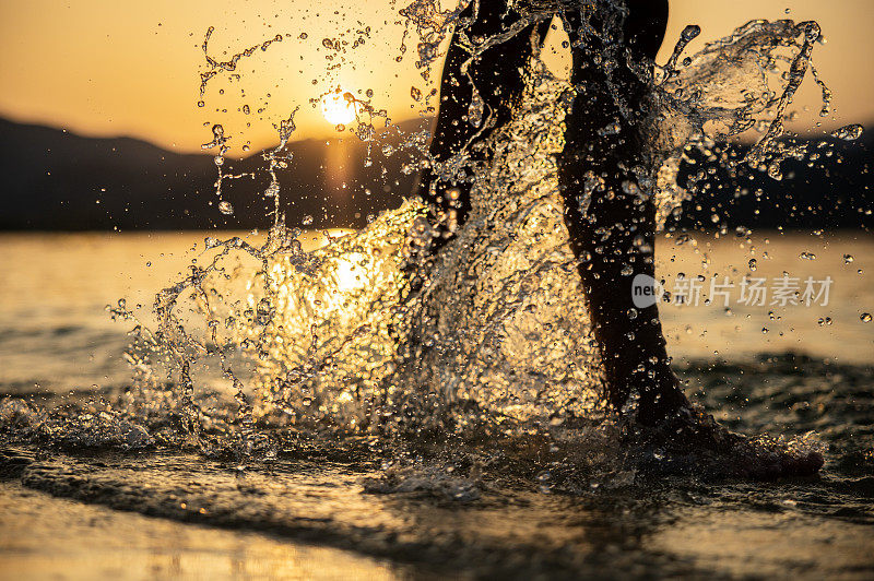 女性的腿走进水中在日落的海滩
