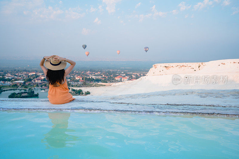 在土耳其德尼兹利的Pamukkale石灰华泳池里，美丽的游客女孩正在观看热气球