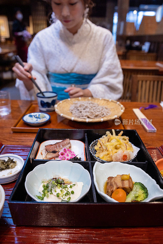 在日本料理店享用精致的日式盘子午餐和荞麦面，穿着和服的女人在那里吃着面条