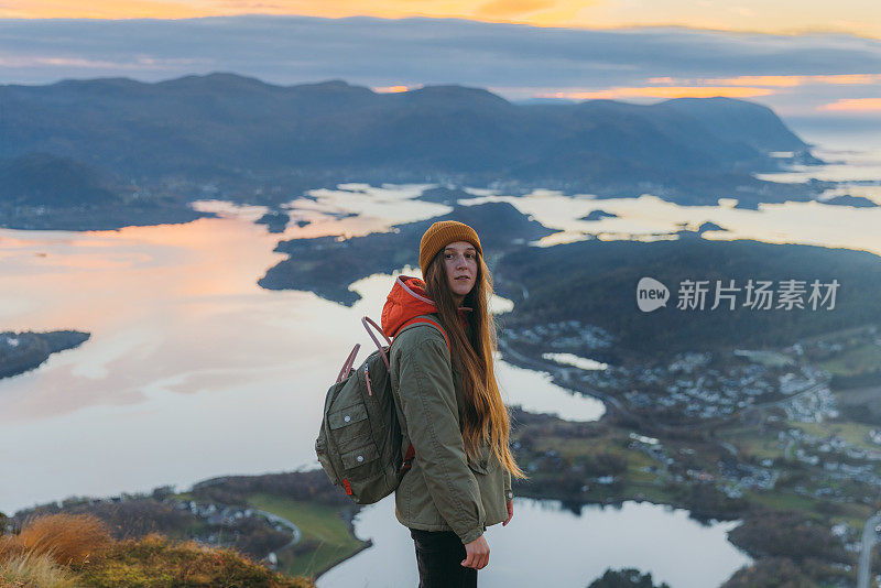 在挪威，一名妇女站在岛屿和大海之上凝视日落