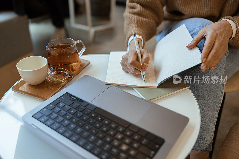 近距离的女人做笔记在笔记本电脑在咖啡馆工作