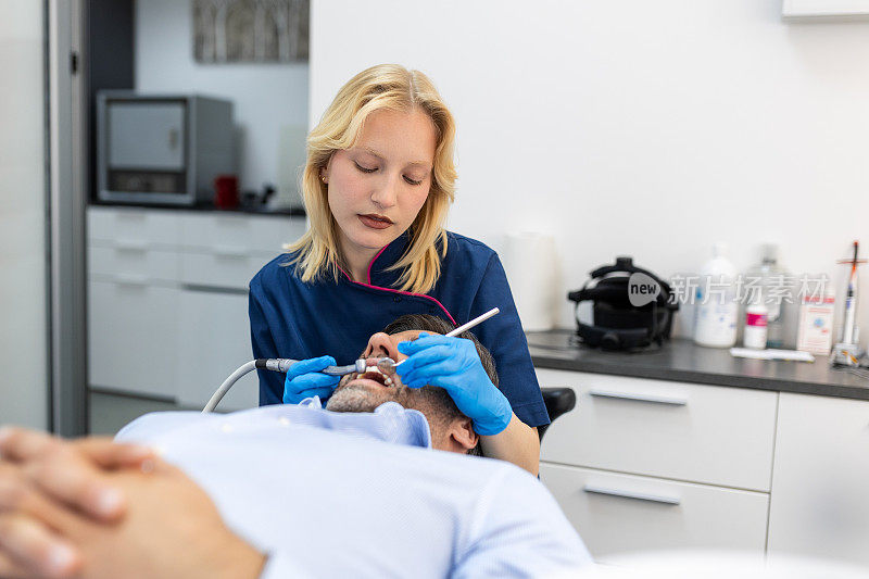 在现代牙科诊所，穿着蓝色制服的牙医正在给患者做牙齿手术，男性患者在治疗过程中
