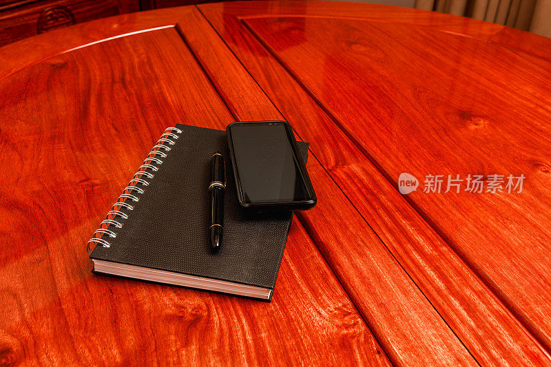 一个笔记本、一支笔和一部手机放在红木桌子上，为商务会议做好准备